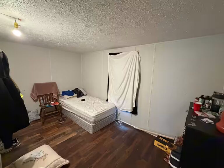 Bedroom with bare mattress on wood floor, sheet-covered window, and a DeWalt box nearby