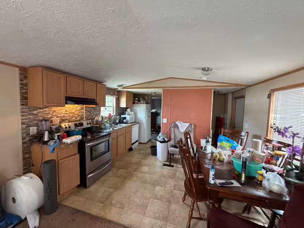 Cluttered kitchen and dining area with wood cabinets, stove, and a dining table covered with items.