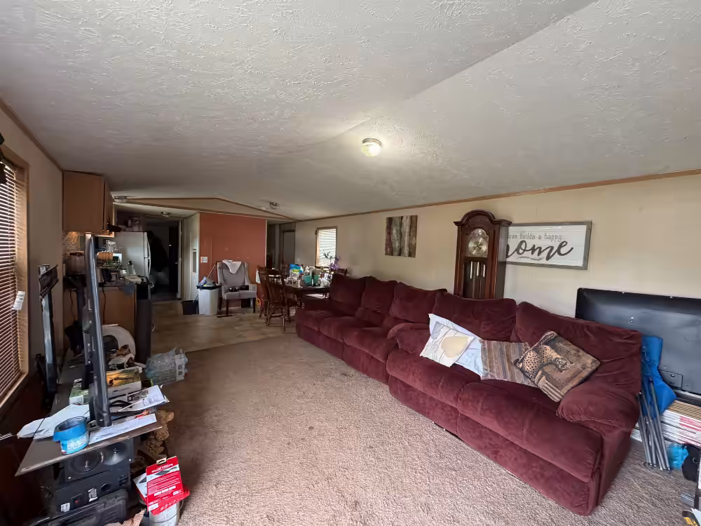 Living room with burgundy sectional sofa, grandfather clock, TV, and "Home" wall sign.