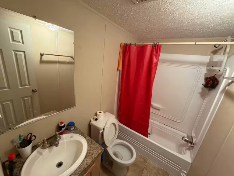 Bathroom with white sink, mirror, toilet, and bathtub with red shower curtain.