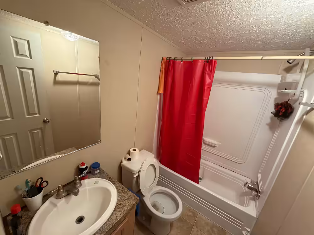 Bathroom with white sink, mirror, toilet, and bathtub with red shower curtain.