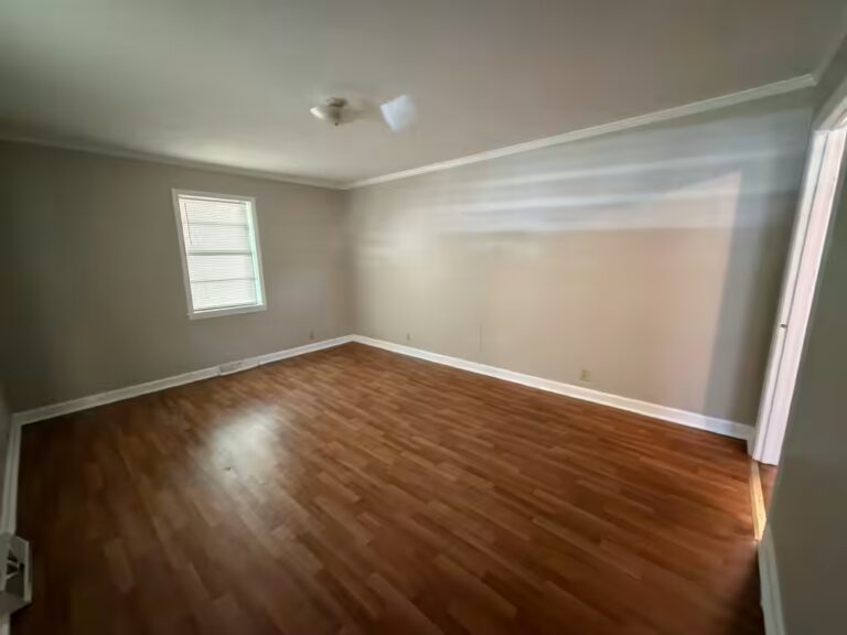 Empty room with hardwood floors, gray walls, window with blinds, and ceiling light fixture